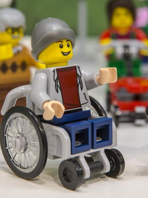 Man sieht eine Lego-Figur. Sie zeigt einen jungen Mann im Rollstuhl, der einen Hund als Assistenz hat.