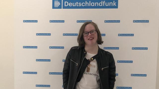 Natalie Dedreux steht vor einer Wand mit Deutschlandfunk-Schriftzügen.