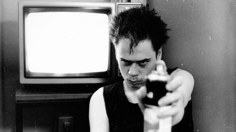 Schwarz-Weiß Aufnahme eines Mannes in schwarzem Tanktop vor einem Fernseher mit einer Sprühflasche in der Hand. Schwarz-Weiß Aufnahme eines Mannes in schwarzem Tanktop vor einem Fernseher mit einer Sprühflasche in der Hand.