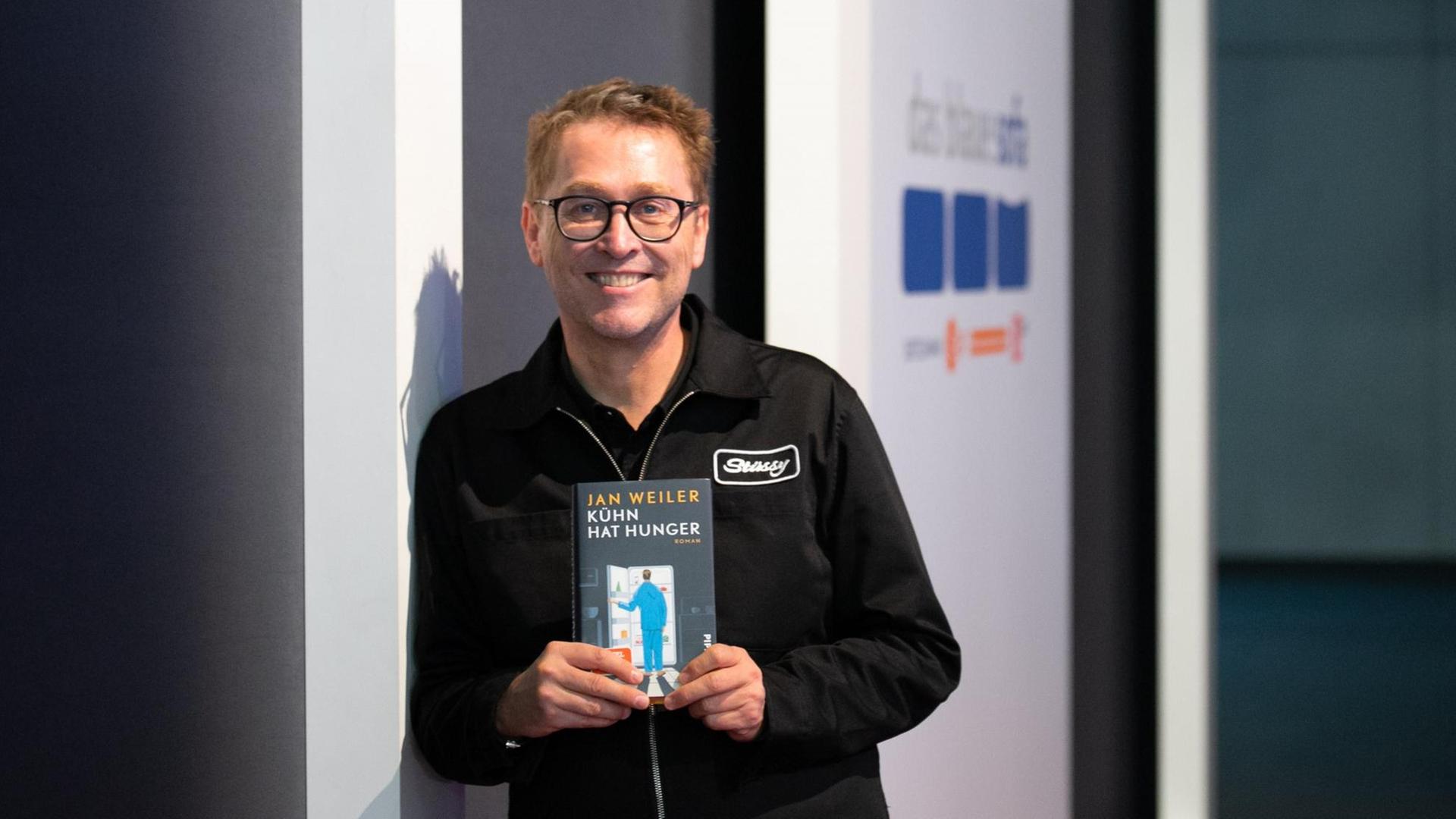 Jan Weiler lehnt an einer Wand mit seinem neuen Buch. Jan Weiler lehnt an einer Wand mit seinem neuen Buch.