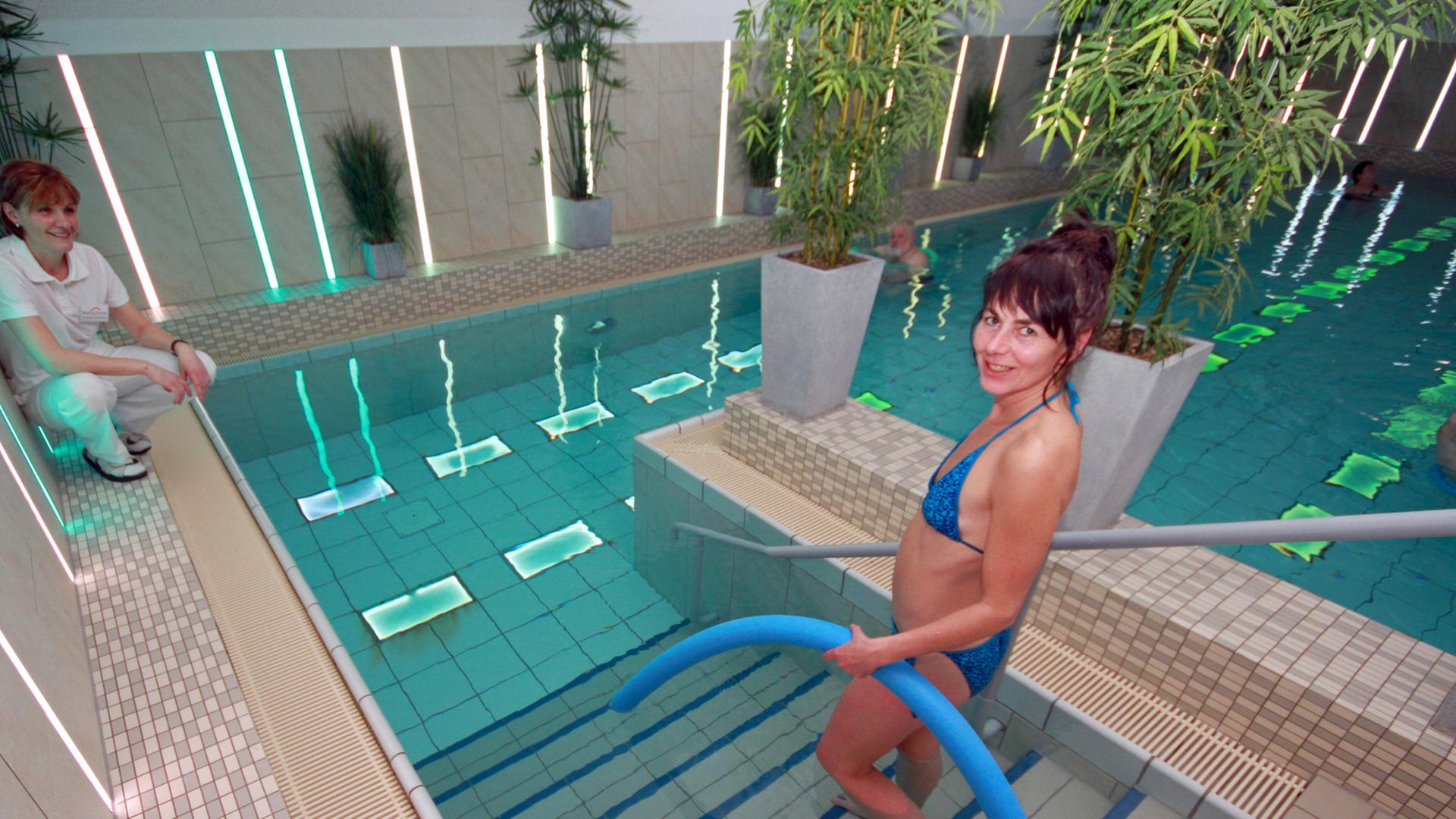 Eine Patientin betritt mit einer Poolnudel in der linken Hand ein Schwimmbad. Eine Patientin betritt mit einer Poolnudel in der linken Hand ein Schwimmbad.