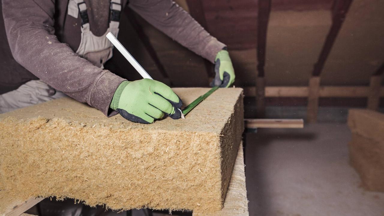 Hände messen Dämmmaterial eines Daches aus beim Bau eines Eigenheims. Hände messen Dämmmaterial eines Daches aus beim Bau eines Eigenheims.