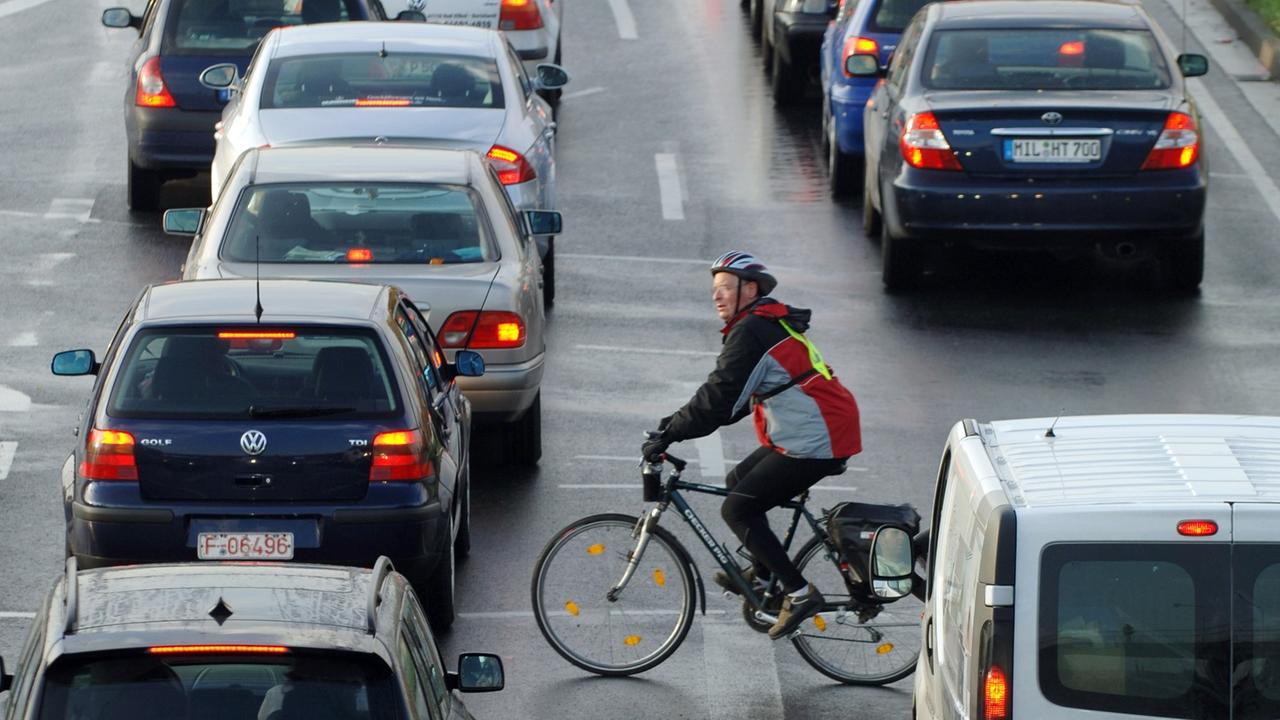 Ein Fahrradfahrer fährt zwischen Autos vorbei, die sich an einer Einfallstraße von Frankfurt am Main im Berufsverkehr stauen. Ein Fahrradfahrer fährt zwischen Autos vorbei, die sich an einer Einfallstraße von Frankfurt am Main im Berufsverkehr stauen.