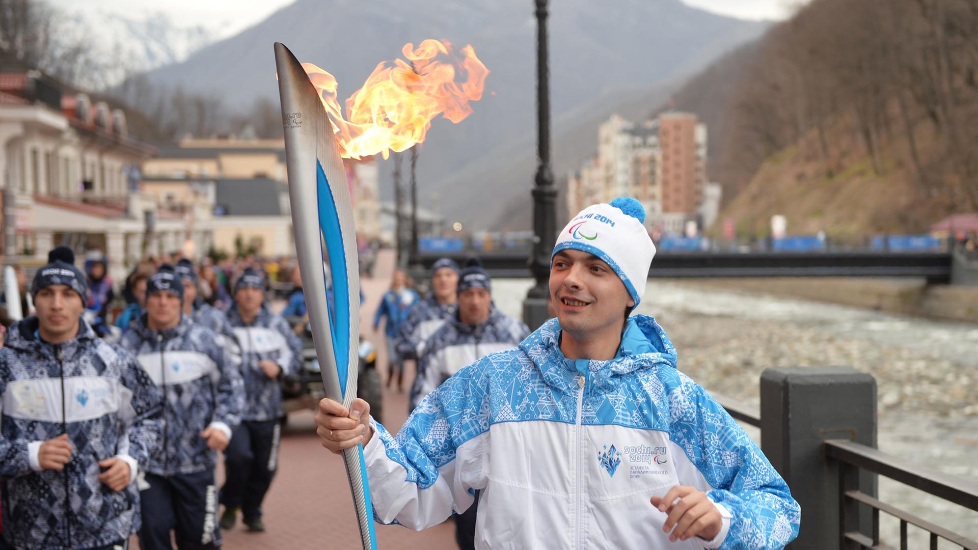 Ein Fackelträger bei den Paralympics in Sotschi, neben ihm dutzende Läufer. Ein Fackelträger bei den Paralympics in Sotschi, neben ihm dutzende Läufer.