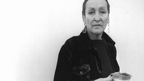 Die Künstlerin Meret Oppenheim 1975 mit eigenen Werken: Tasse und Teller mit Pelz überzogen und ein Kohlenobjekt