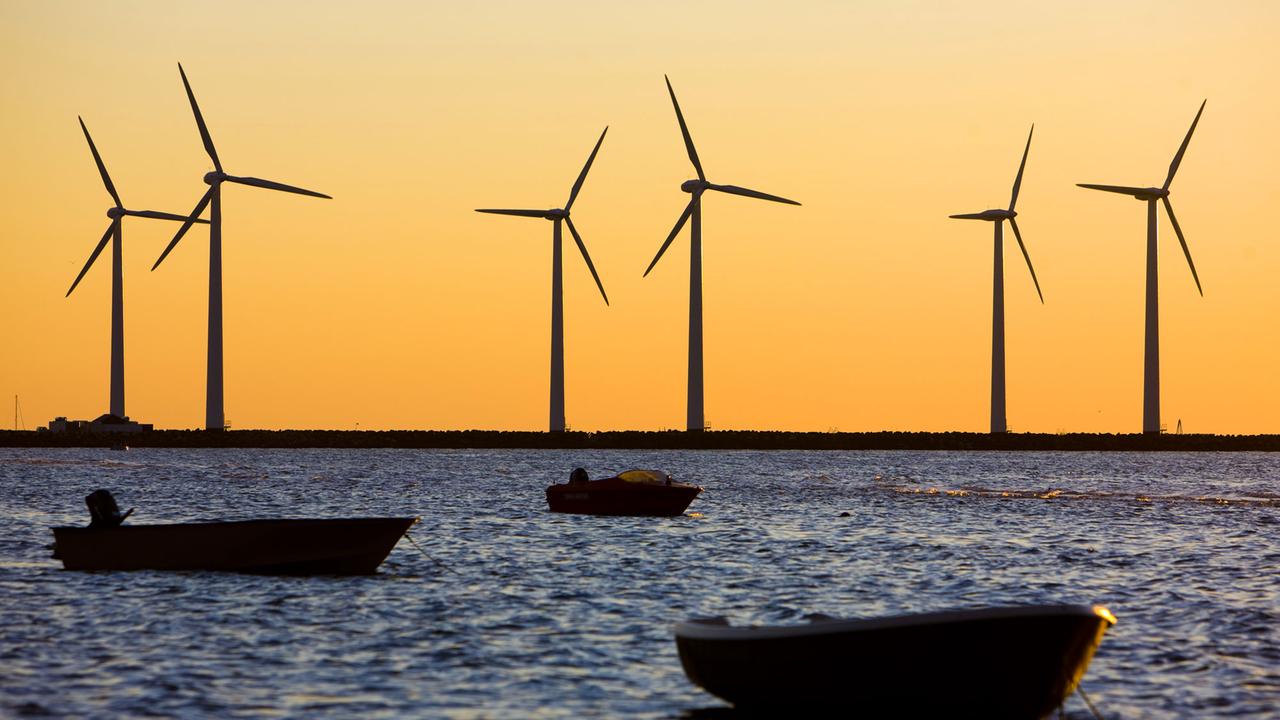 Windräder drehen sich bei Sonnenuntergang vor dem Abendhimmel auf der Mole der dänischen Gemeinde Bonnerup in der nordöstlichen Ecke von Djursland auf der Ostsee.