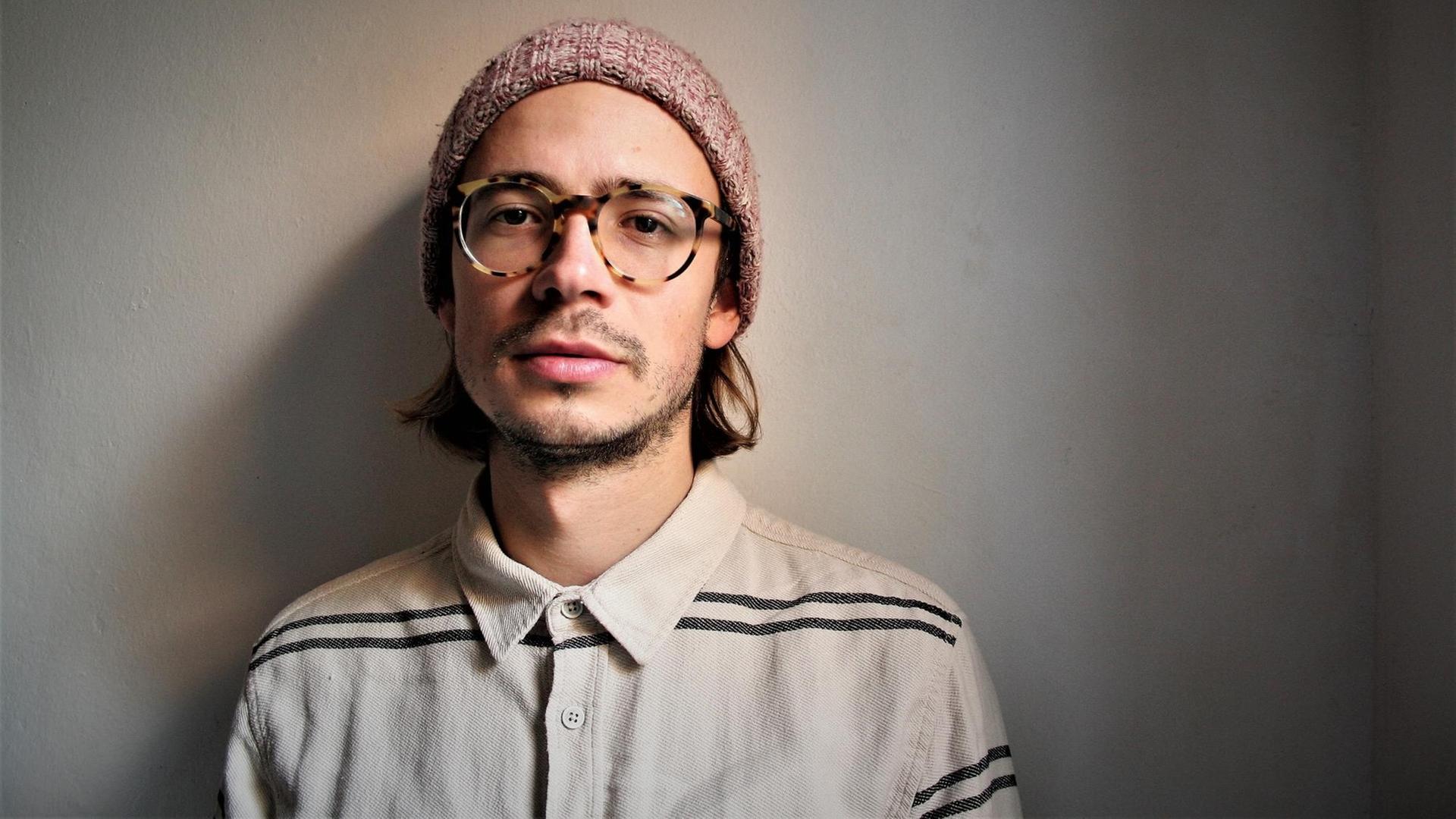 Der Pianist Jonathan Hofmeister steht vor einem grauen Hintergrund Der Pianist Jonathan Hofmeister steht vor einem grauen Hintergrund