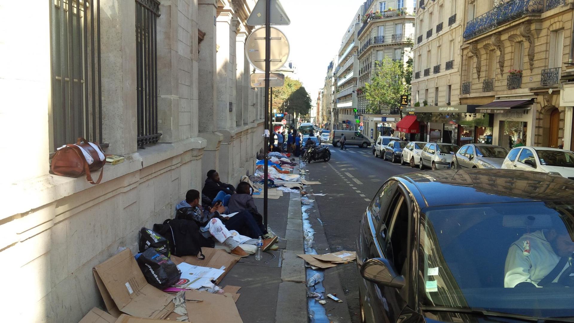 Flüchtlinge aus Eritrea, Sudan und dem Tschad sitzen auf Pappkartons auf einem schmutzigen Bürgersteig in Paris.