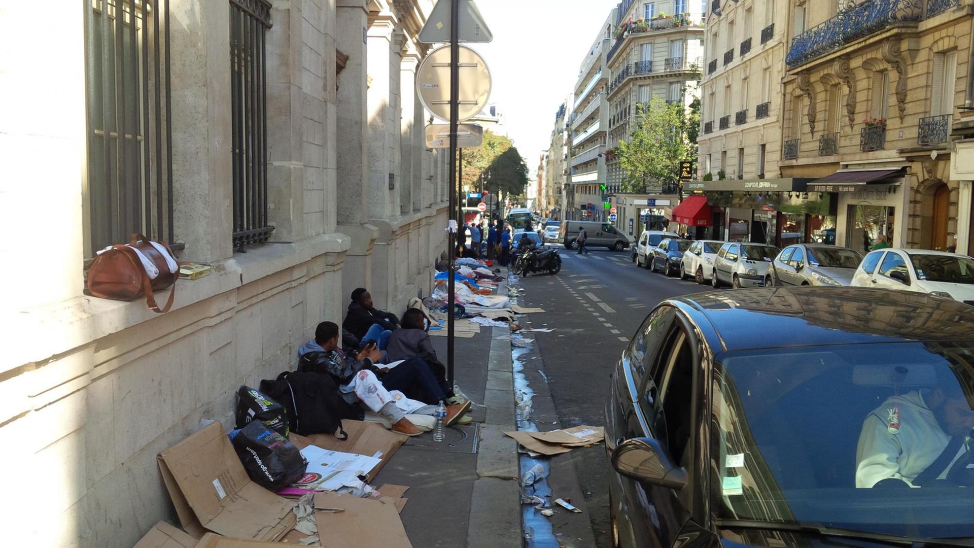 Flüchtlinge aus Eritrea, Sudan und dem Tschad sitzen auf Pappkartons auf einem schmutzigen Bürgersteig in Paris. Flüchtlinge aus Eritrea, Sudan und dem Tschad sitzen auf Pappkartons auf einem schmutzigen Bürgersteig in Paris.