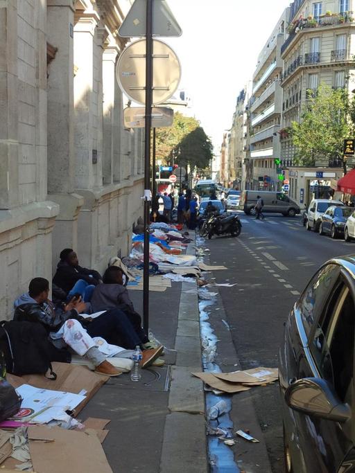 Flüchtlinge aus Eritrea, Sudan und dem Tschad sitzen auf Pappkartons auf einem schmutzigen Bürgersteig in Paris.
