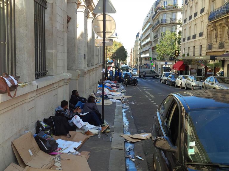 Flüchtlinge aus Eritrea, Sudan und dem Tschad sitzen auf Pappkartons auf einem schmutzigen Bürgersteig in Paris.