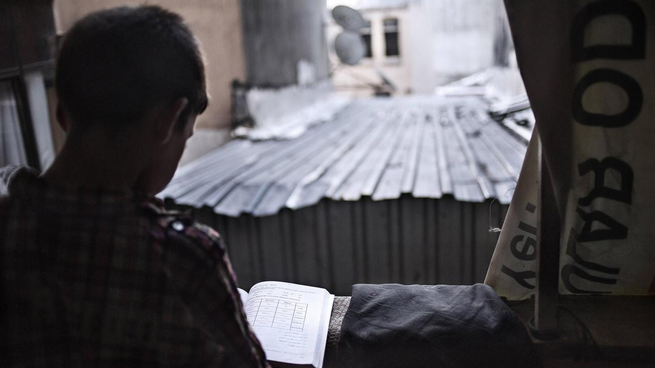 Ein syrisches Kind liest ein Schulbuch.