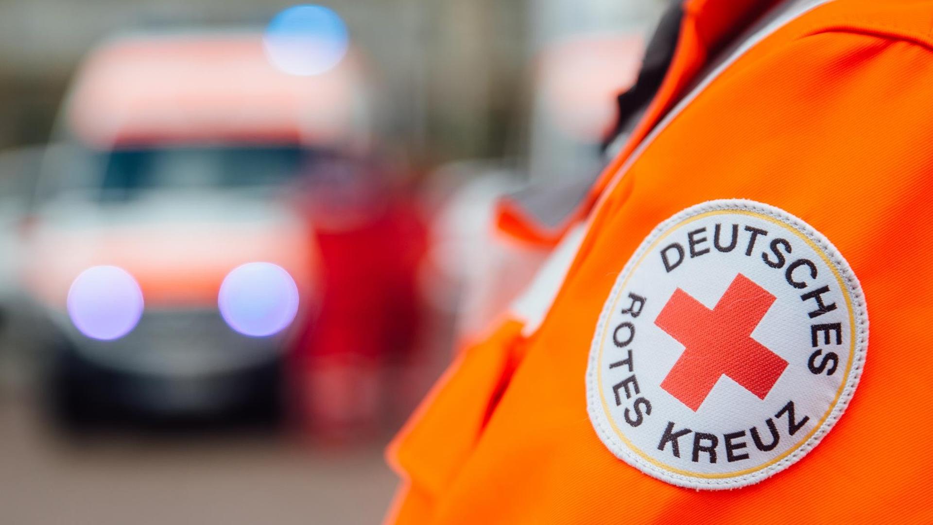 Ein Arm mit einem Aufnäher mit der Aufschrift "Deutsches Rotes Kreuz" ist vor einem Rettungsfahrzeug zu sehen.