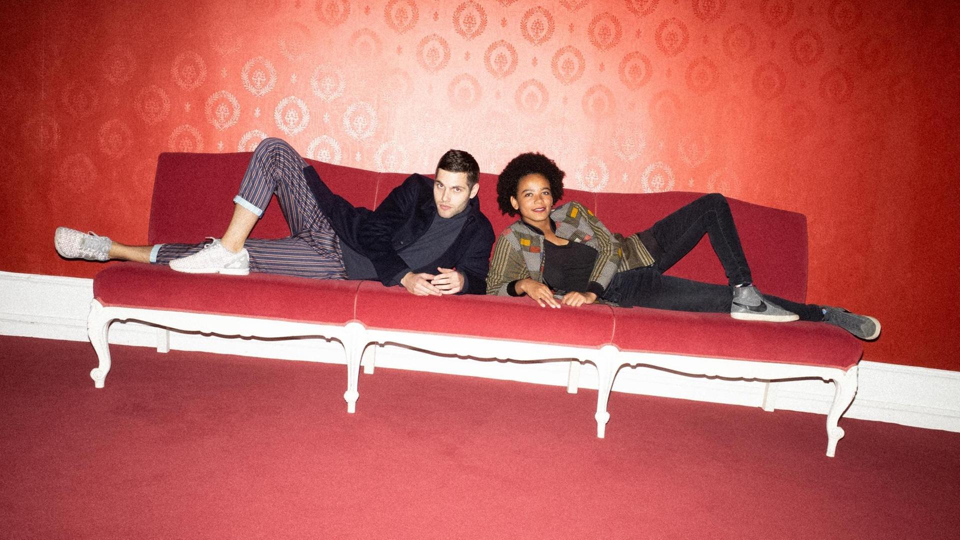 Porträt von Fatima Moumouni und Laurin Buser, sie liegen auf einem roten Sofa Porträt von Fatima Moumouni und Laurin Buser, sie liegen auf einem roten Sofa