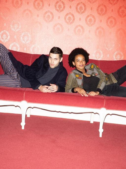 Porträt von Fatima Moumouni und Laurin Buser, sie liegen auf einem roten Sofa