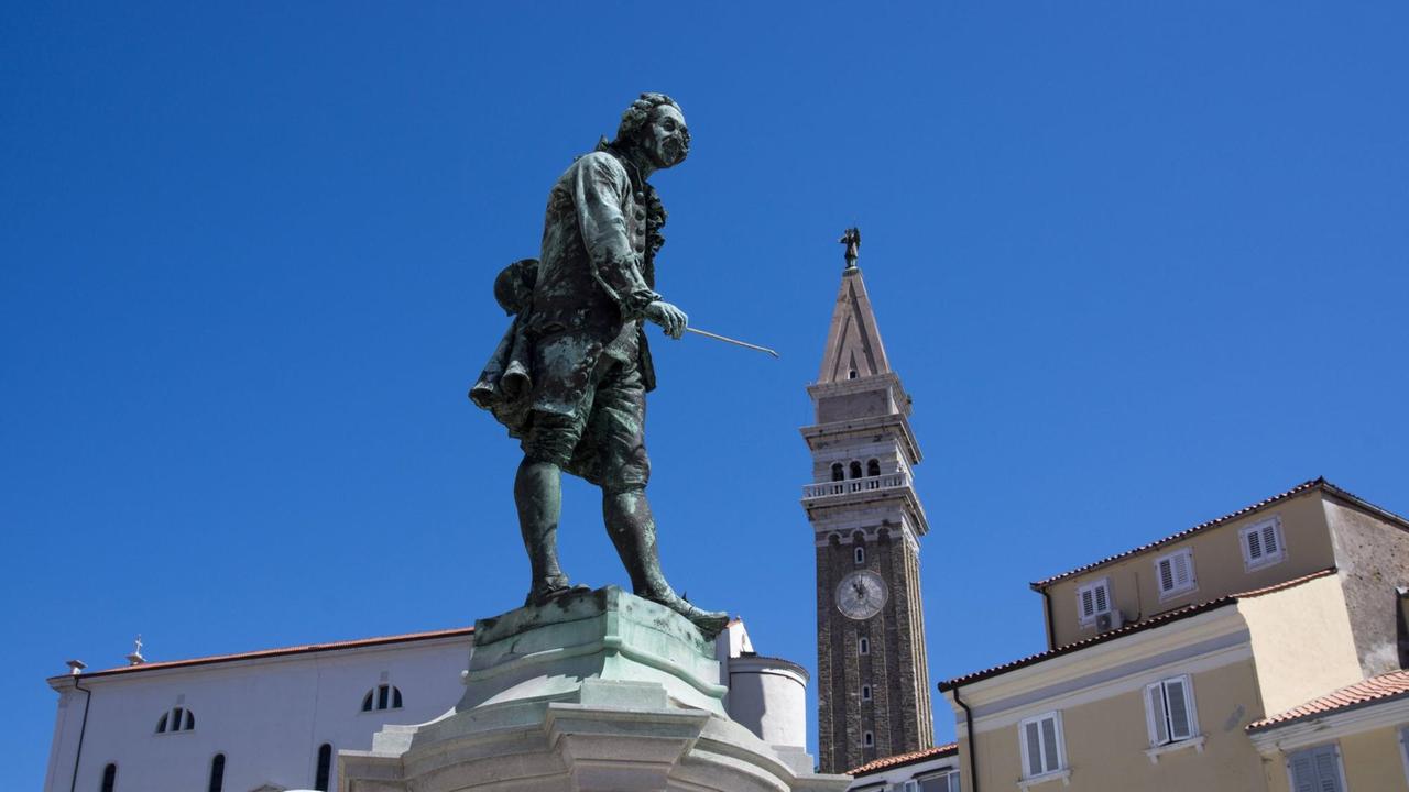 Blick auf die Statue des Geigers, dessen Geigenbogen zu einer Kirche im Hintergrund weist.