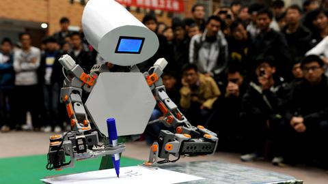 Ein Roboter schreibt etwas, während eine Menschenmenge hinter ihm stehend dabei zuschaut.
