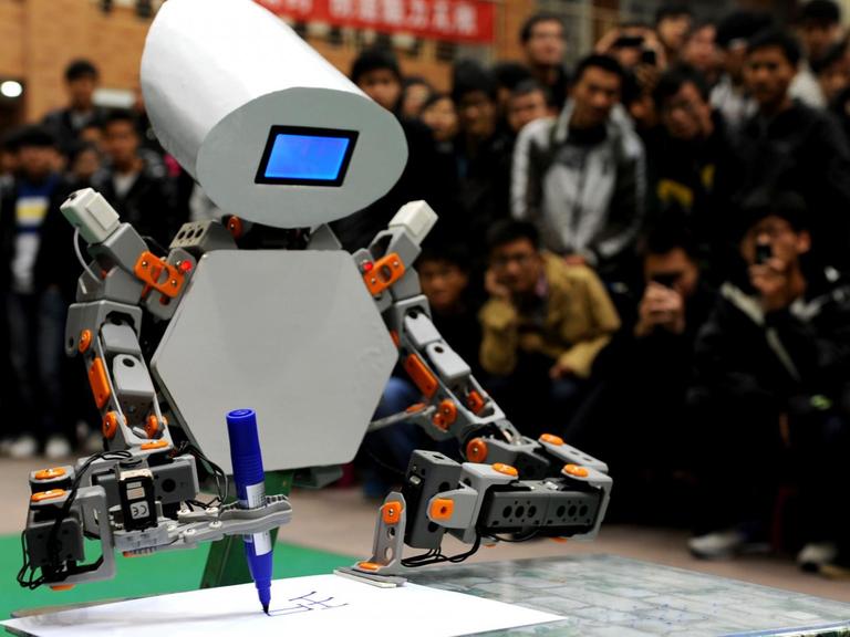 Ein Roboter schreibt etwas, während eine Menschenmenge hinter ihm stehend dabei zuschaut.