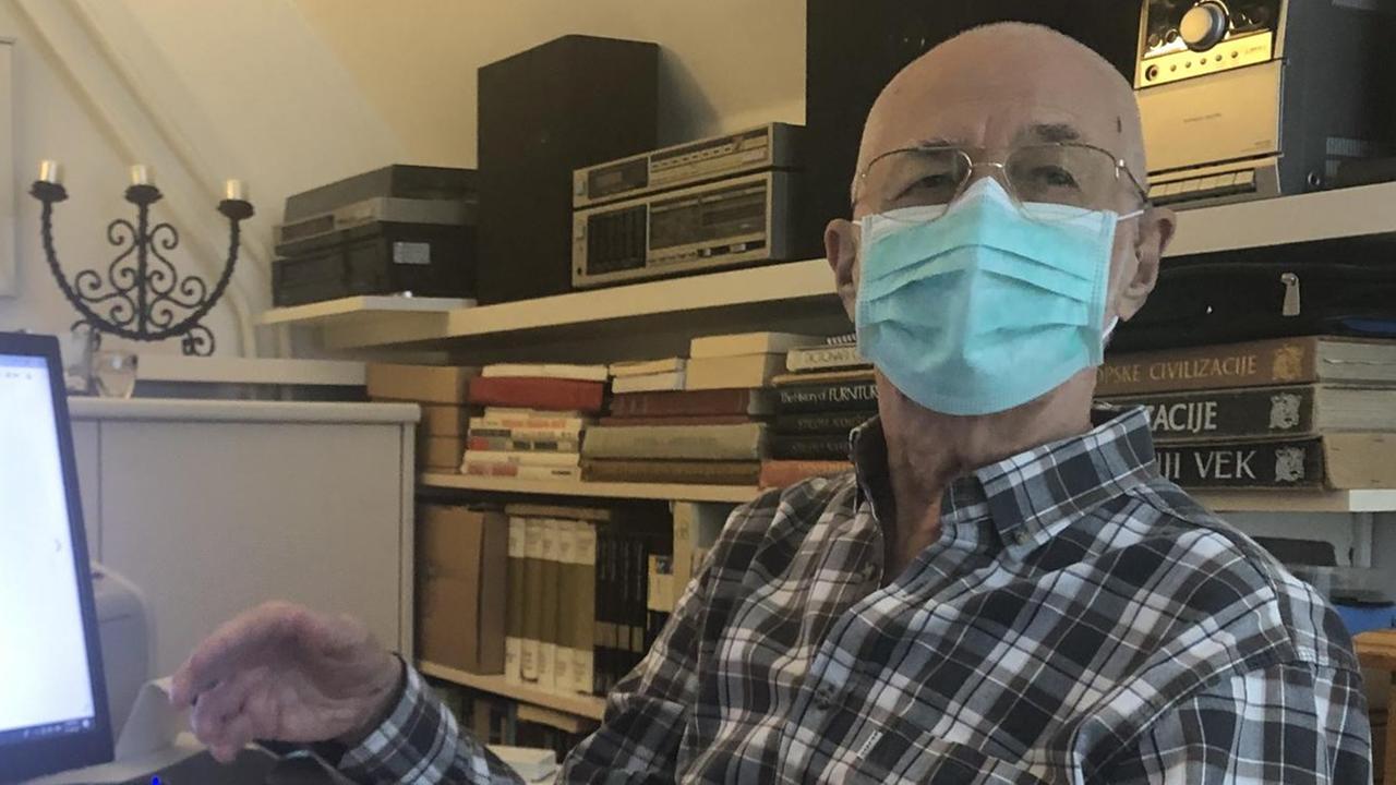 Ein Mann mit Maske sitzt in einer Wohnung vor einem Rechner. Ein Mann mit Maske sitzt in einer Wohnung vor einem Rechner.