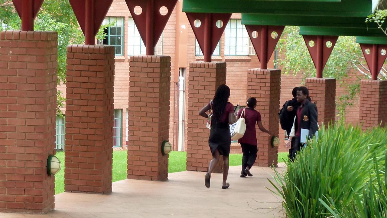 Schülerinnen laufen mit ihren Unterrichtsmaterialien durch einen offenen Gang zu ihren Klassenräumen.