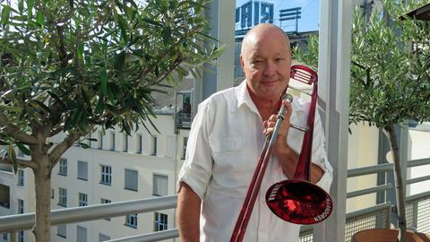 Der schwedische Jazzmusiker Nils Landgren steht mit seinem Markenzeichen, der roten Posaune, auf der Dachterasse von Deutschlandfunk Kultur.