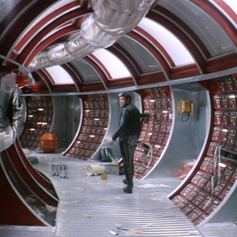 Ein Mann steht im futuristisch anmutenden Gang eines Raumschiffs.