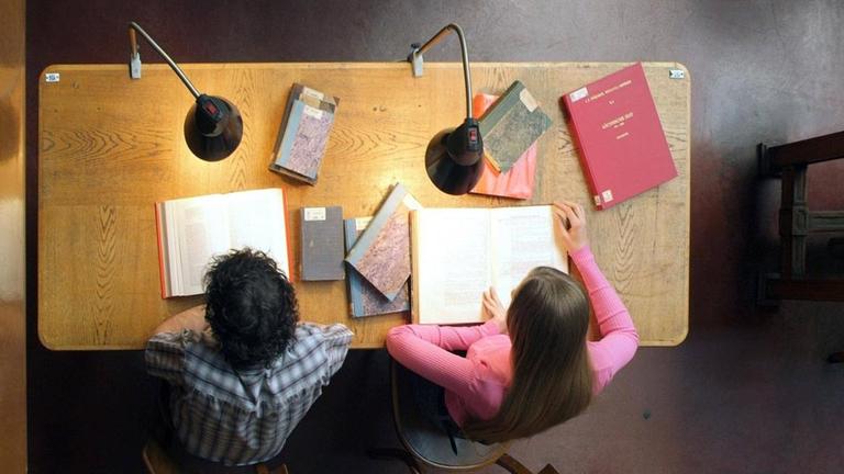 Studenten sitzen an Tisch in Universitätsbibliothek, Blick von oben. Studenten sitzen an Tisch in Universitätsbibliothek, Blick von oben.