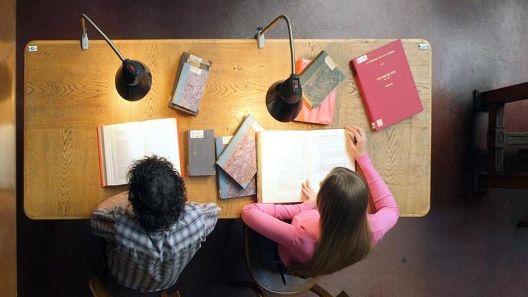 Studenten sitzen an Tisch in Universitätsbibliothek, Blick von oben. Studenten sitzen an Tisch in Universitätsbibliothek, Blick von oben.