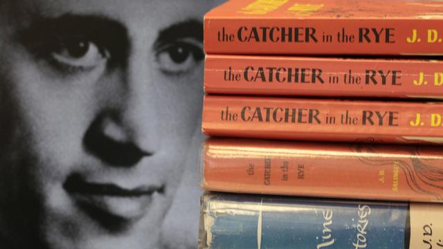 Das Gesicht des Schriftstellers J.D.Salinger neben aufgestapelten Büchern seines Klassikers "Der Fänger im Roggen".
