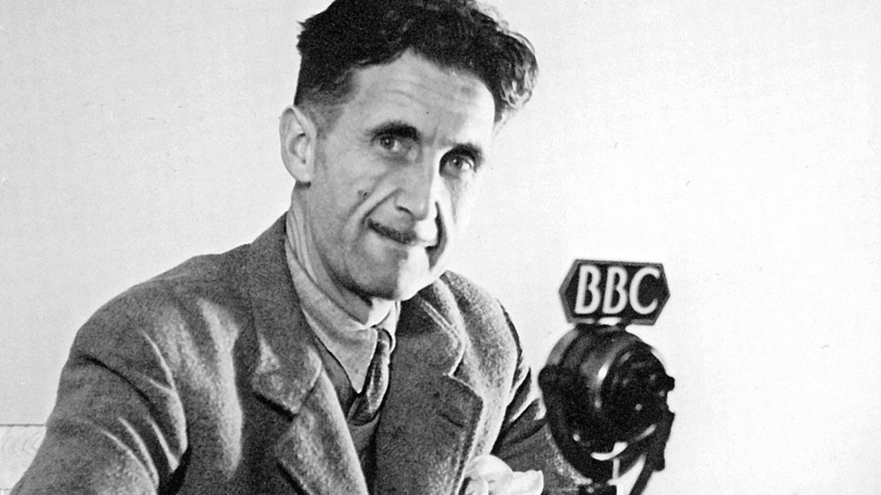 George Orwell sitzt an einem Mikrofon der BBC und blickt in die Kamera. George Orwell sitzt an einem Mikrofon der BBC und blickt in die Kamera.