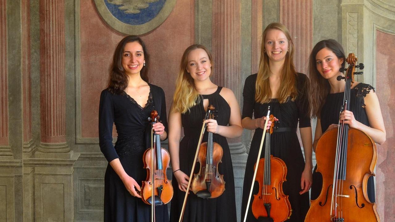 Die vier Musikerinnen stehen in einem historischen Raum in edler, schwarzer Konzertrobe. Die vier Musikerinnen stehen in einem historischen Raum in edler, schwarzer Konzertrobe.