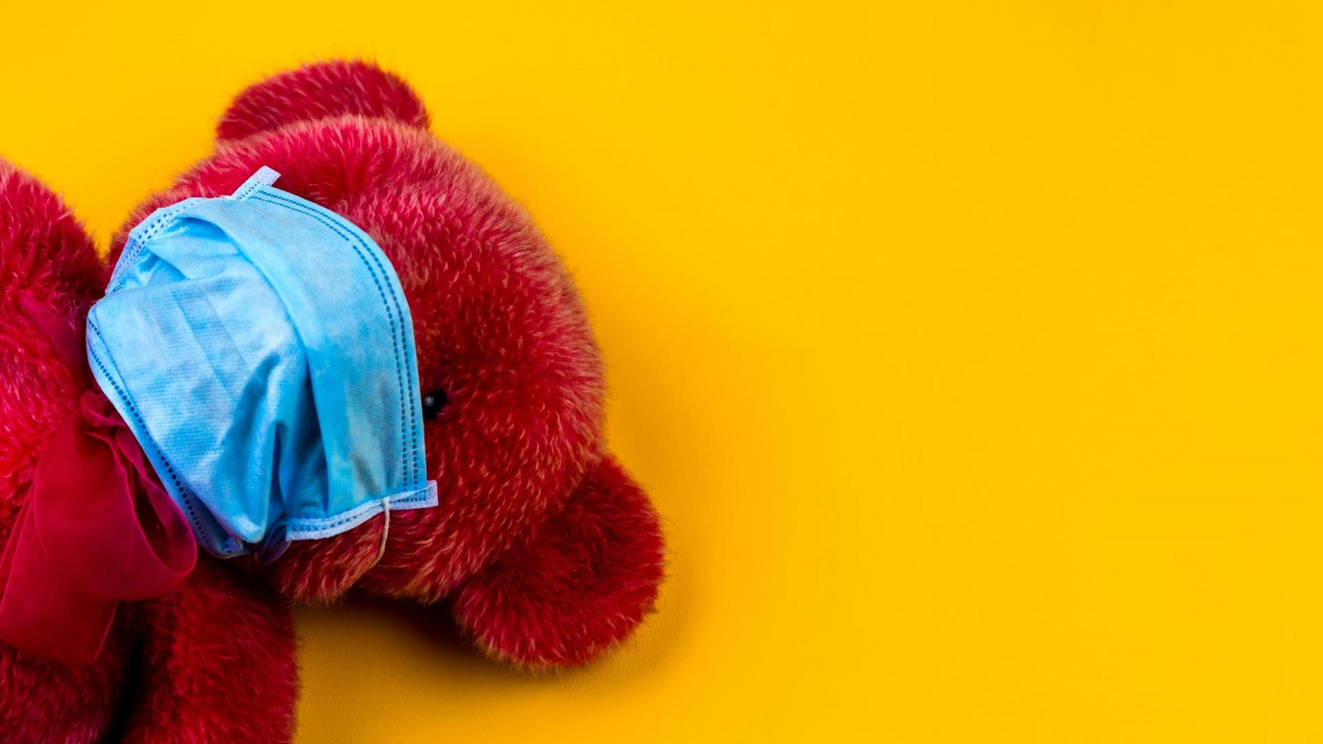 Ein roter Teddybärmit Mundschutz vor gelbem Hintergrund. Ein roter Teddybärmit Mundschutz vor gelbem Hintergrund.