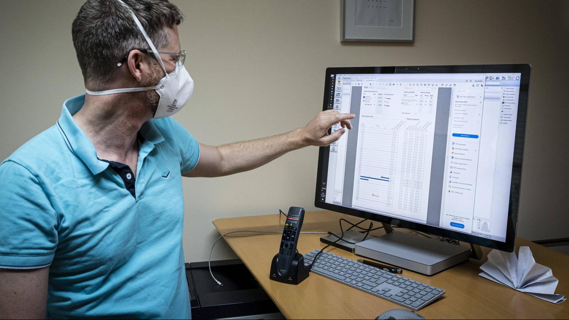 Ein Arzt mit FFP2-Maske zeigt auf einen Monitor mit Patientendaten Ein Arzt mit FFP2-Maske zeigt auf einen Monitor mit Patientendaten