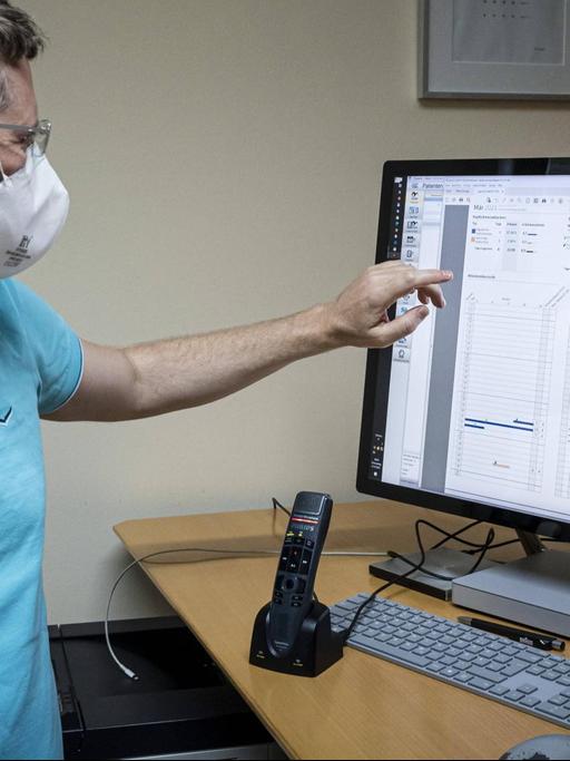 Ein Arzt mit FFP2-Maske zeigt auf einen Monitor mit Patientendaten