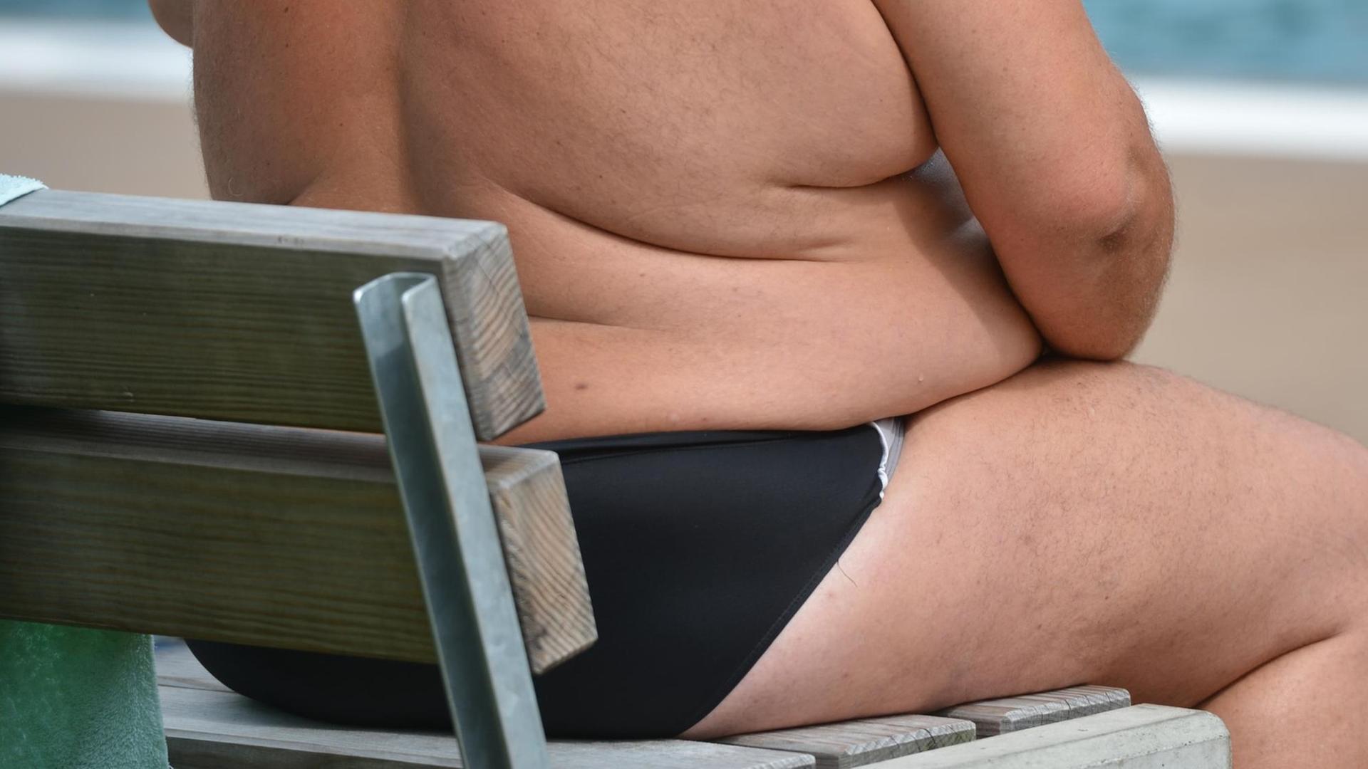 Ein übergewichtiger Mensch sitzt am 18.08.2016 in einem Freibad in Stuttgart (Baden-Württemberg). Foto: Franziska Kraufman/dpa | Verwendung weltweit