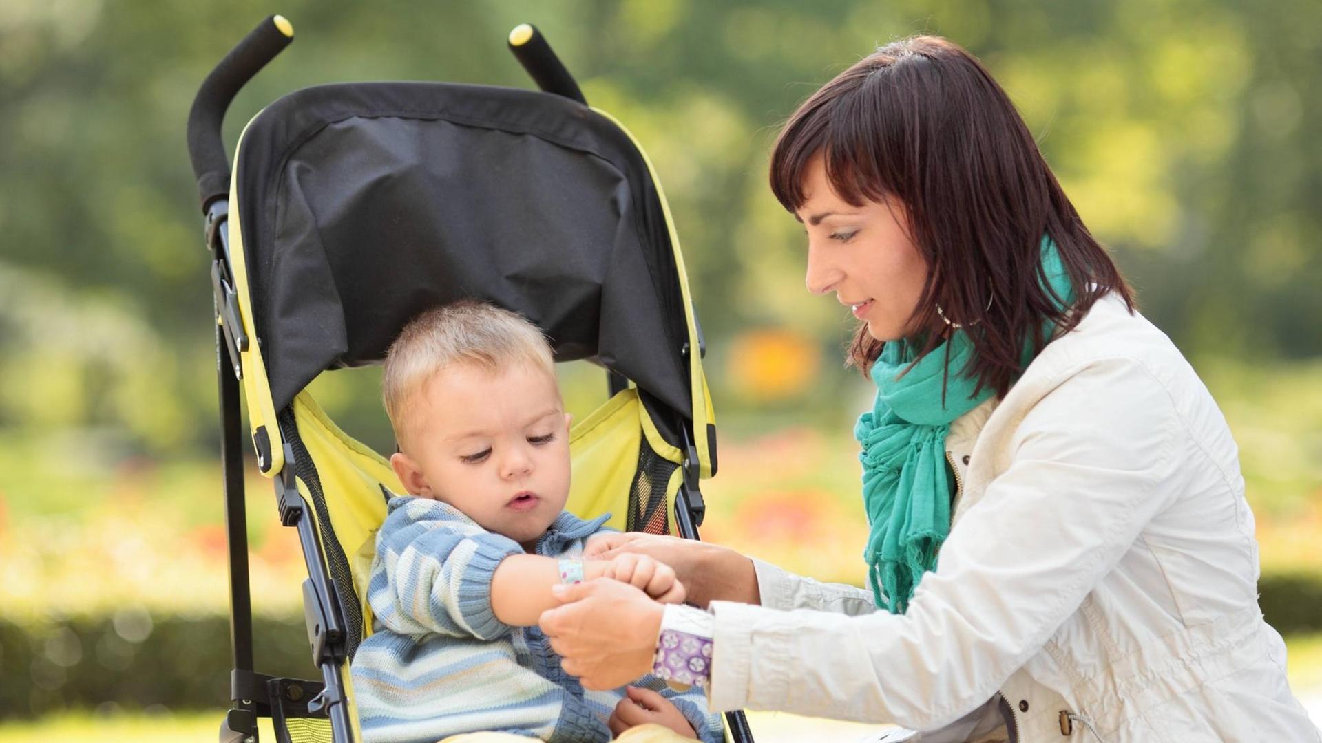 Eine Mutter kümmert sich in einem Park um ihren Sohn im Kinderwagen. Eine Mutter kümmert sich in einem Park um ihren Sohn im Kinderwagen.