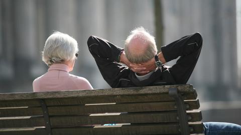 Ein Rentnerpaar sitzt auf einer Bank vor dem Reichstag in Berlin und sonnt sich.