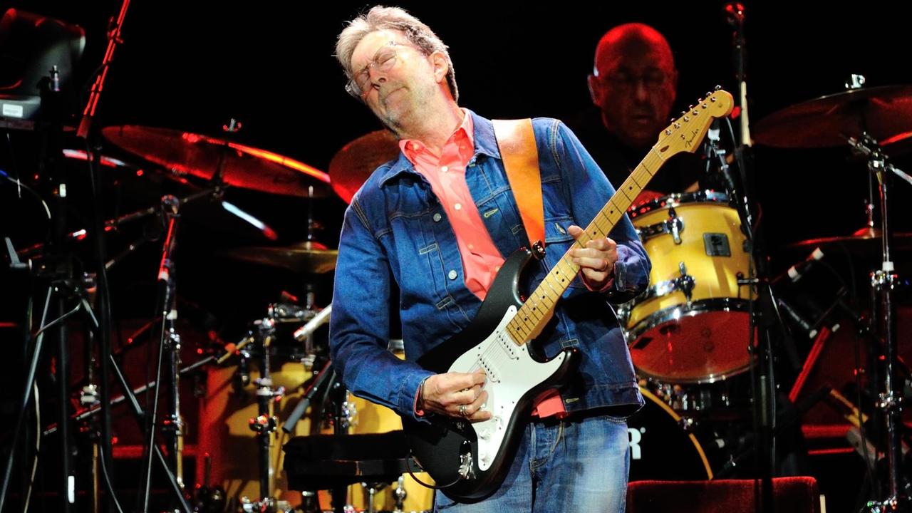 Ein Mann steht vor einem Schlagzeug auf einer Bühne und spielt mit geschlossenen Augen Elektrogitarre. Ein Mann steht vor einem Schlagzeug auf einer Bühne und spielt mit geschlossenen Augen Elektrogitarre.