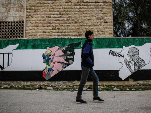 Das Foto zeigt ein am 14. März 2021 in Idlib aufgenommene Straßenszene. Ein Passant vor Wandmalereien von Aktivisten zum Gedenken an den zehnten Jahrestag der syrischen Revolution in Nordsyrien, die unter der Kontrolle der syrischen Opposition ist.