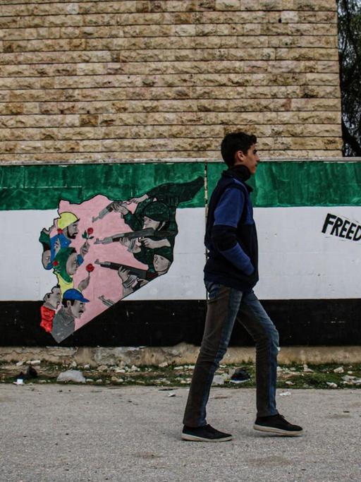 Das Foto zeigt ein am 14. März 2021 in Idlib aufgenommene Straßenszene. Ein Passant vor Wandmalereien von Aktivisten zum Gedenken an den zehnten Jahrestag der syrischen Revolution in Nordsyrien, die unter der Kontrolle der syrischen Opposition ist.