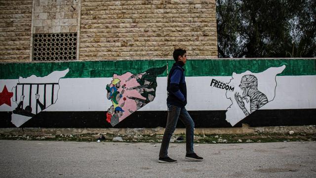 Das Foto zeigt ein am 14. März 2021 in Idlib aufgenommene Straßenszene. Ein Passant vor Wandmalereien von Aktivisten zum Gedenken an den zehnten Jahrestag der syrischen Revolution in Nordsyrien, die unter der Kontrolle der syrischen Opposition ist.