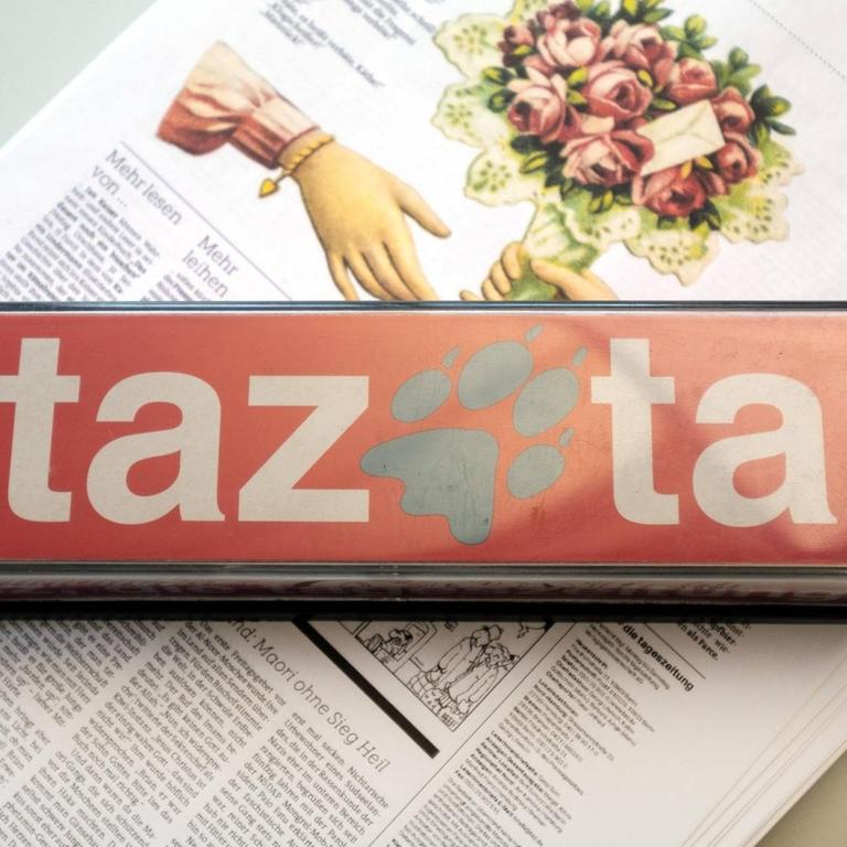 Ein Briefbeschwerer mit "taz"-Logo liegt auf einer Ausgabe der Zeitung.
