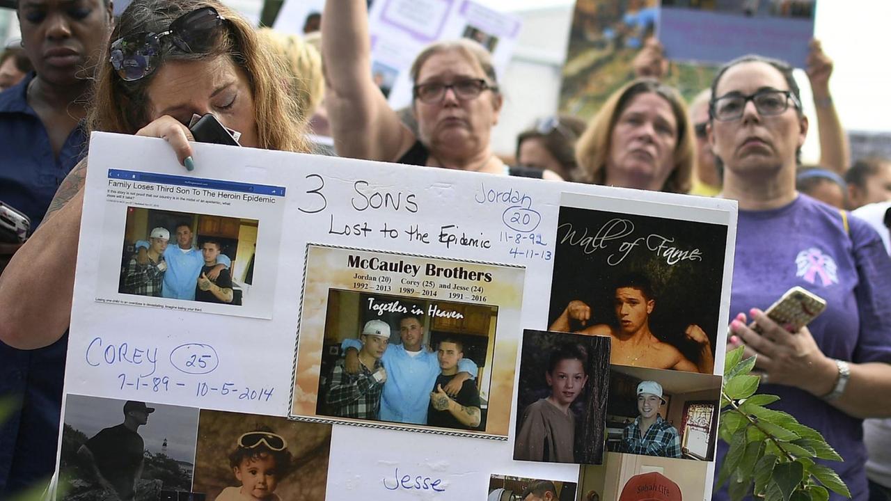 Eine Frau hält im August 2018 vor der Firmenzentrale von "Purdue Pharma" in Stamford, Conneticut, ein Plakat hoch, auf dem drei ihrer Söhne zu sehen sind, die aufgrund des Konsums von Heroien gestorben sind. Eine Frau hält im August 2018 vor der Firmenzentrale von "Purdue Pharma" in Stamford, Conneticut, ein Plakat hoch, auf dem drei ihrer Söhne zu sehen sind, die aufgrund des Konsums von Heroien gestorben sind.