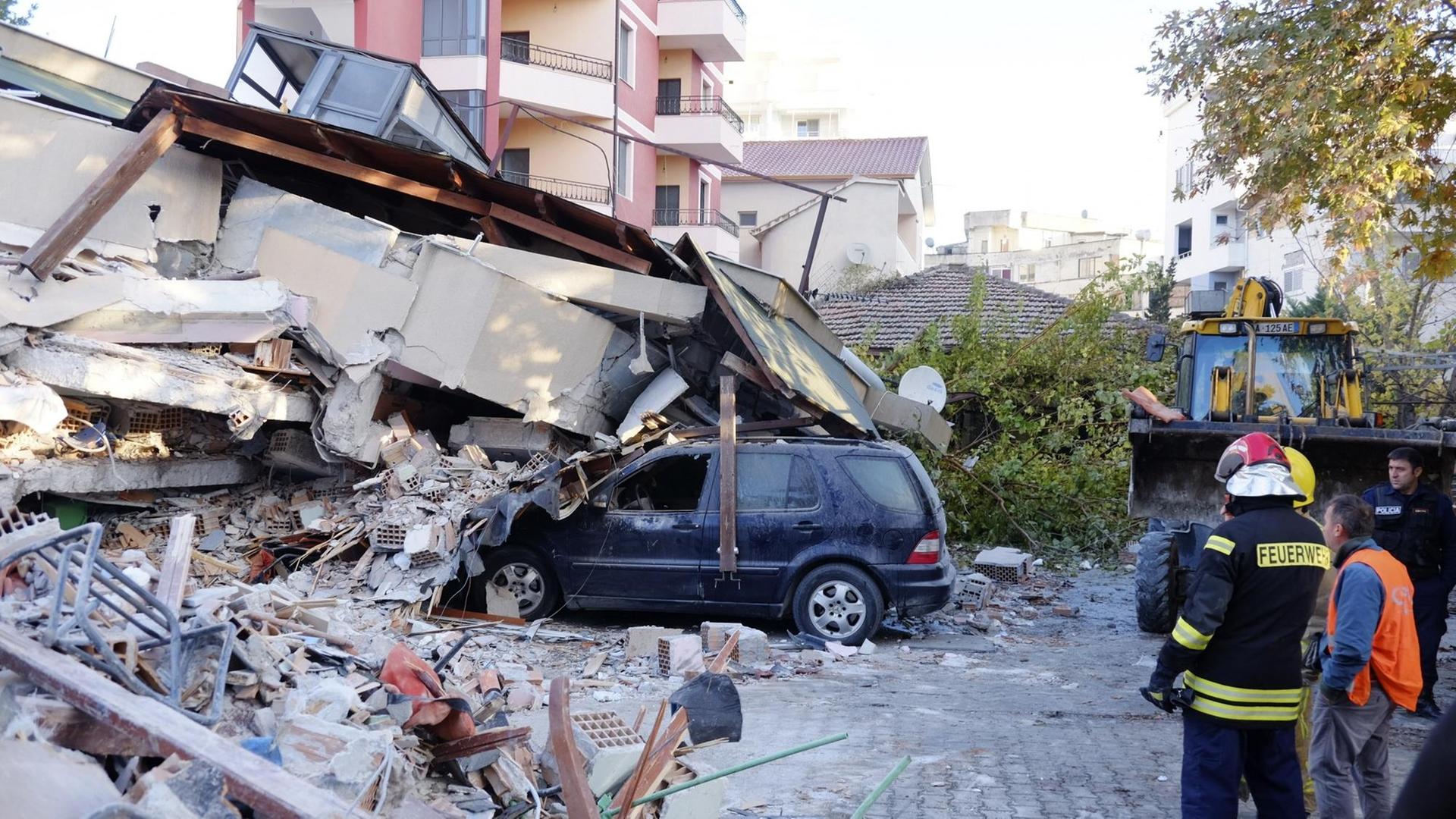 Feuerwehrleute stehen nach einem Erdbeben in Westalbanien neben einem eingestürzten Gebäude, das zum Teil auf ein Auto gestürzt ist.