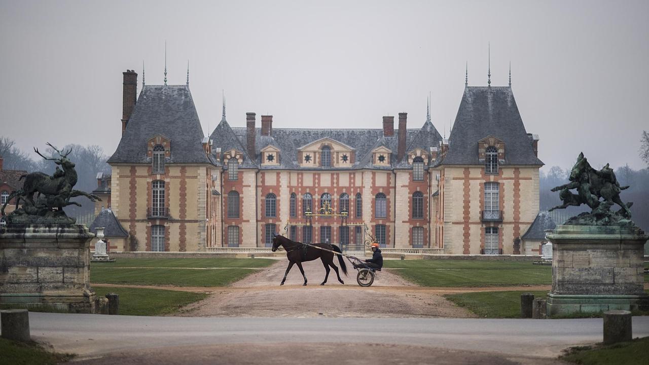 Ein Trabrennpferd und sein Reiter im Sulky laufen vor dem Schloss von Grobois in Frankreich entlang