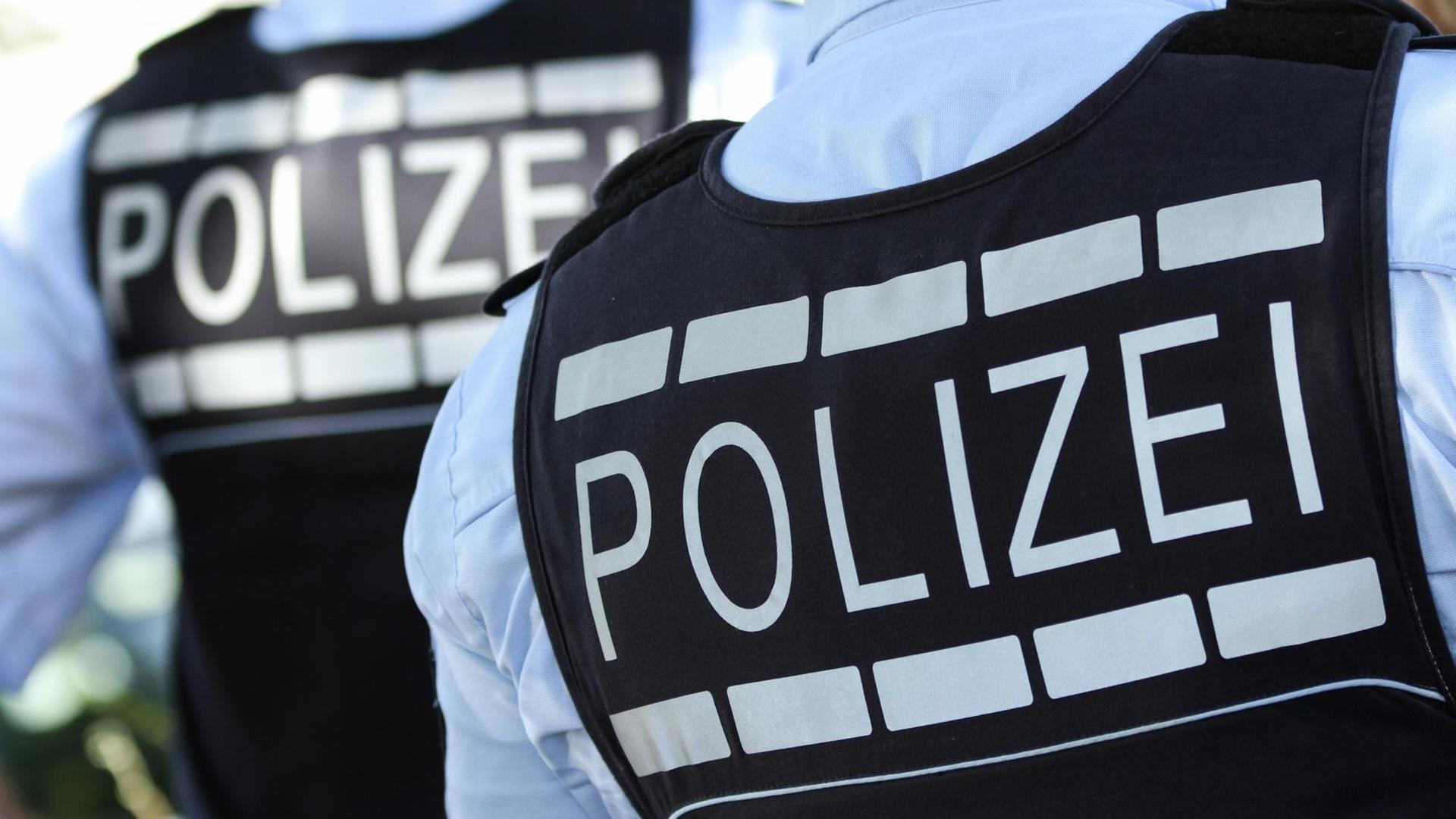 Die Rückansicht von zwei Polizistenwesten zeigen die Aufschrift "Polizei"