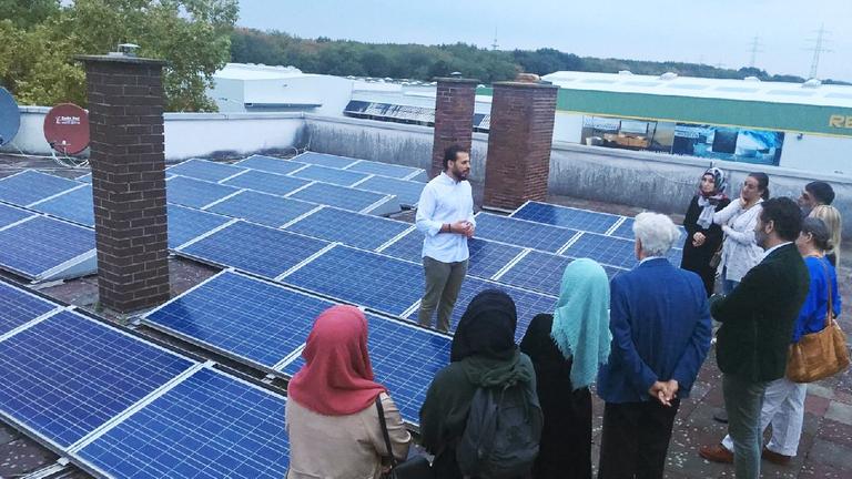 Ein muslimische Gruppe aus Frauen und Männern schaut sich eine Solaranlage auf dem Dach an. Ein muslimische Gruppe aus Frauen und Männern schaut sich eine Solaranlage auf dem Dach an.