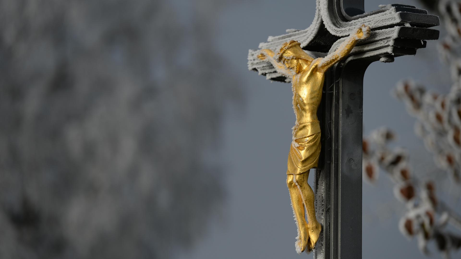 Ein Metallkreuz mit einer goldenen Christusfigur mit einem dünnen Schleier von Frost Ein Metallkreuz mit einer goldenen Christusfigur mit einem dünnen Schleier von Frost