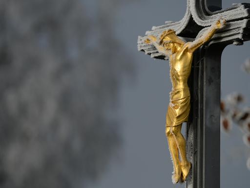 Ein Metallkreuz mit einer goldenen Christusfigur mit einem dünnen Schleier von Frost