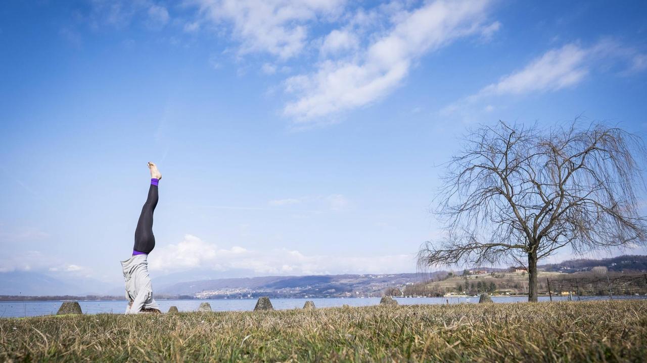 Eine Frau beim Yoga-Kopfstand am See Eine Frau beim Yoga-Kopfstand am See